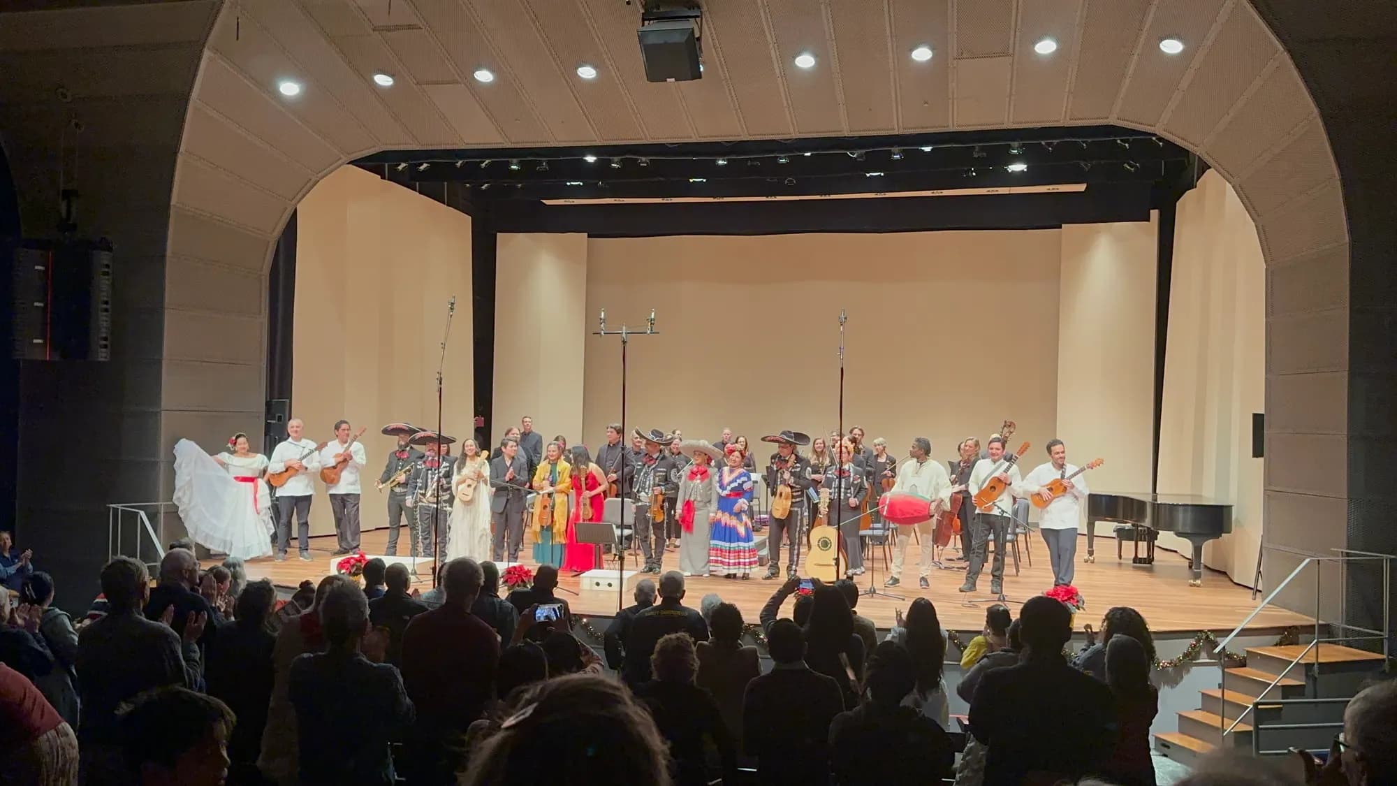 La Orquesta UNIDOS, mariachi y bailarines folclóricos saludando ante una sala llena