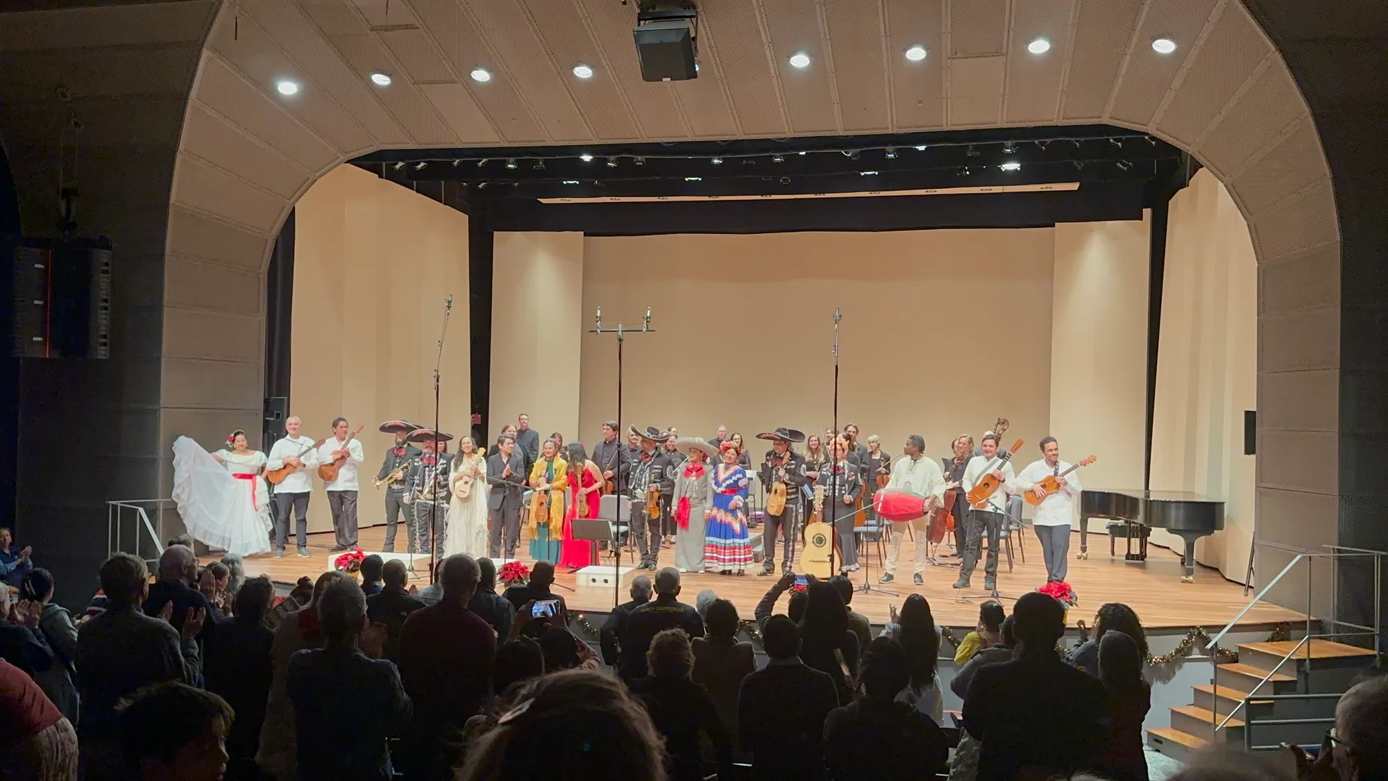 La Orquesta UNIDOS, mariachi y bailarines folclóricos saludando ante una sala llena